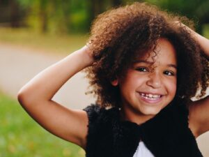 Photo by Eye for Ebony girl wearing black vest raising two hands near green grass field during daytime